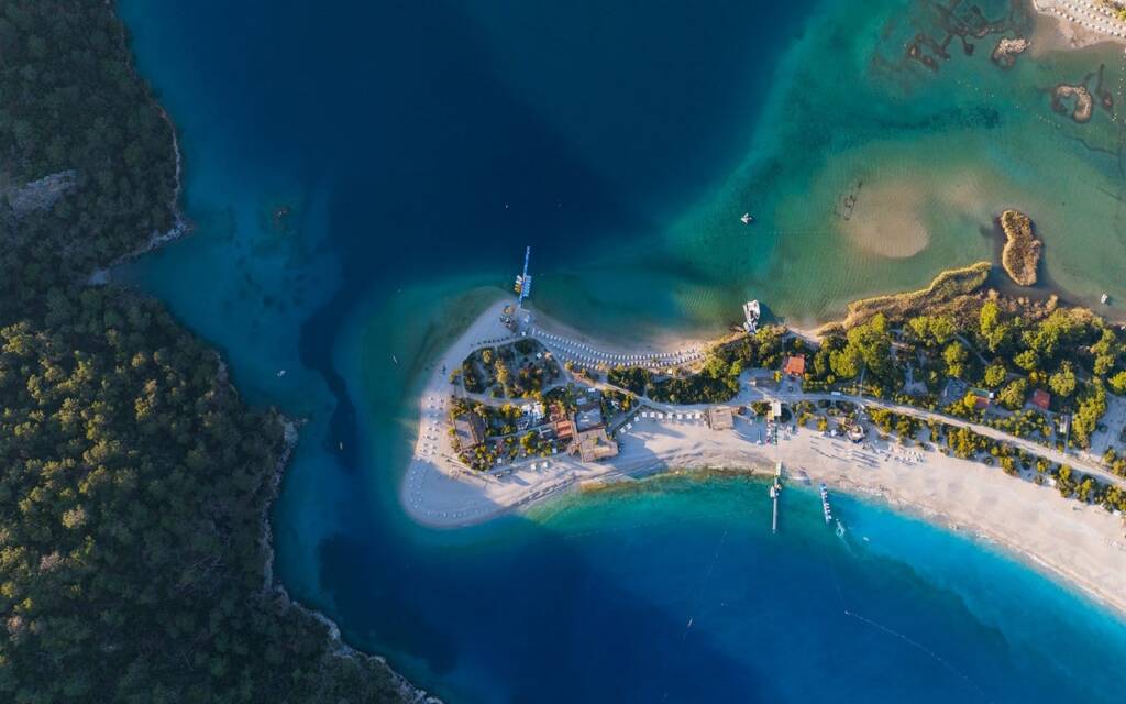Breathtaking aerial view of Ölüdeniz beach in Fethiye, Turkey, showcasing turquoise waters, lush green mountains, and a long sandy beach.
