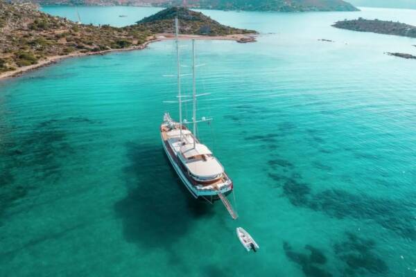 A majestic Gulet Halcon Del Mar anchored in a turquoise bay, surrounded by lush green hills and crystal-clear waters.