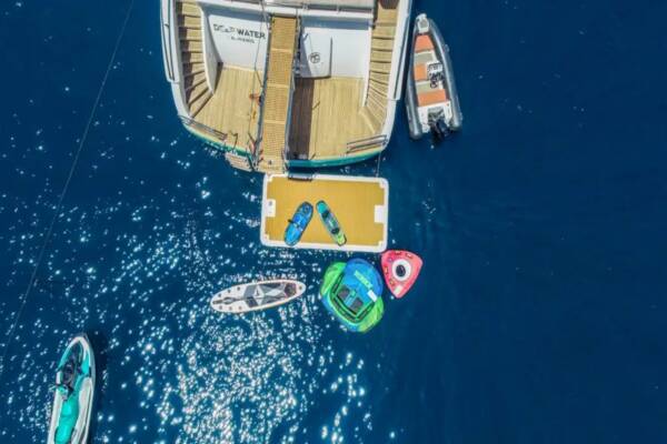 People enjoying various water toys like jet skis, paddleboards, and inflatables, off the deck of a luxurious gulet yacht anchored in a picturesque Turkish bay.
